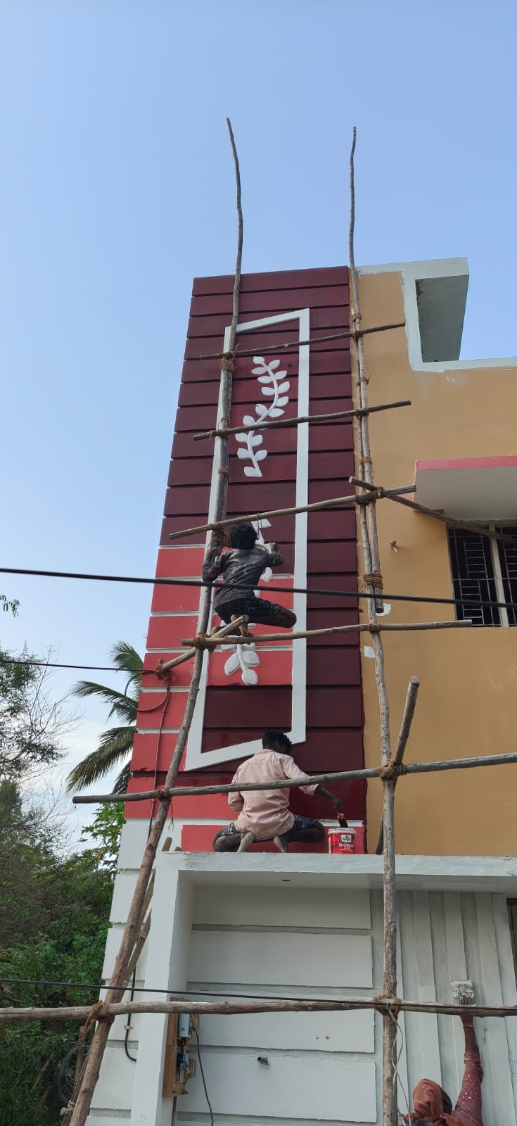 Workers applying decorative maroon and leaf motif paint on G+2 home facade with bamboo scaffolding, Mannarkudi